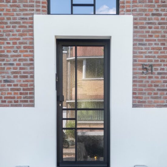 De buitendeur is vervaardigd uit hoogwaardig zwart aluminium, voorzien van een Reynaers SL 38 profiel dat bekend staat om zijn stevige en slanke lijnen. De deur beschikt over slanke profielen die een eigentijdse uitstraling geven, terwijl de zwarte afwerking zorgt voor een strakke en moderne look. Het ontwerp combineert de stijl van een moderne steel look met subtiele klassieke elementen, waardoor het geheel een tijdloze uitstraling krijgt. Deze aluminium buitendeur straalt zowel kracht als elegantie uit, en past perfect in een eigentijdse woning met een vleugje klassieke charme. Het resultaat is een stijlvolle, duurzame deur die indruk maakt door zijn slanke profiel en verfijnde uitstraling.