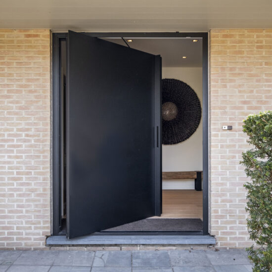Een moderne zwarte aluminium pivotdeur van Reynaers, uitgevoerd in hoogwaardig aluminium. Deze deur combineert vakmanschap met een strak design, waardoor een stijlvolle aansluiting ontstaat tussen interieur en buitenruimte. Dankzij het sterke materiaal en de innovatieve pivot-techniek biedt de deur duurzaamheid en functionaliteit. De strakke lijnen en moderne uitstraling maken het een eyecatcher van elke moderne woning.